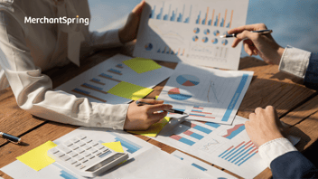 Close-up of two professionals reviewing printed charts, graphs, and financial reports with a calculator and notes on the table, symbolizing business analysis and operational planning