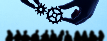 Silhouetted hands connecting two gears above a blurred group of people, symbolizing teamwork, alignment, and the integration of vendor strategies and negotiations
