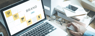 Open laptop displaying a digital brand strategy layout with icons, next to a person’s hand on a computer mouse