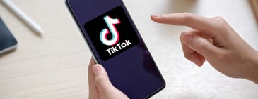 Person holding a smartphone displaying the TikTok logo on screen, representing social media engagement and e-commerce opportunities on TikTok Shop