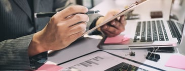 Business professional reviewing charts and data on a clipboard beside a laptop, symbolising revenue balance and diversification strategy